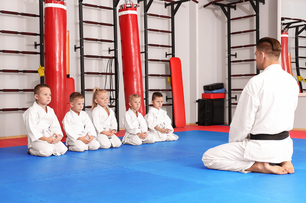 instructor teaching children sat on martial arts mat